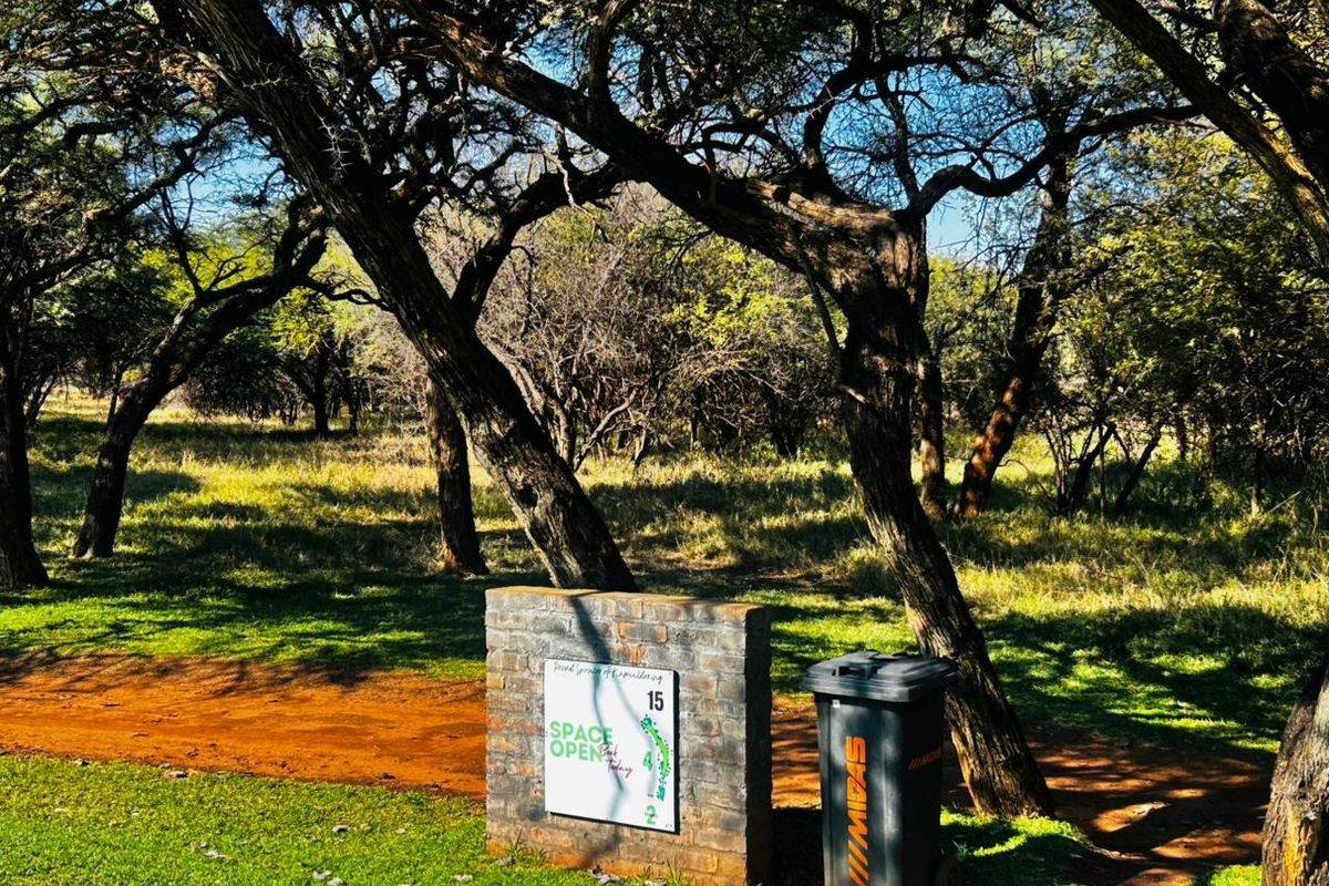 A view of a residential vacant land plot featuring a brick signage pillar and mature trees on a grassed verge.