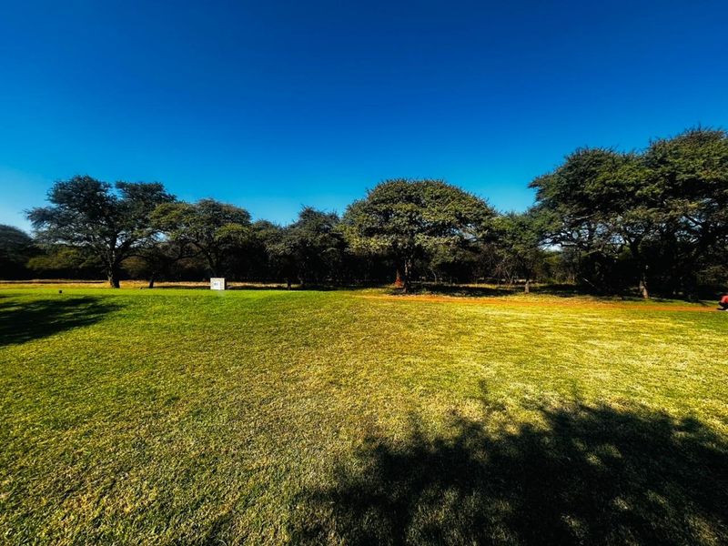 A spacious, well-maintained grassy plot featuring mature trees, offering a peaceful and open outdoor setting.