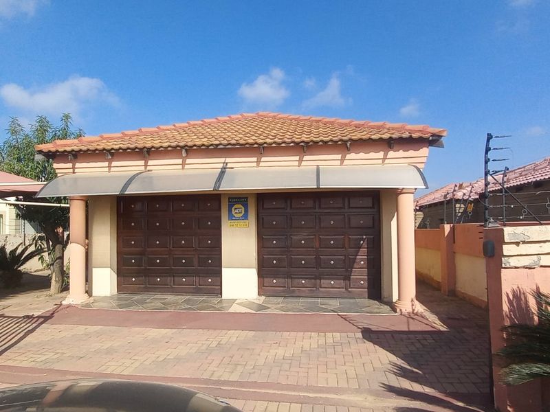 A detached double garage featuring a tiled roof, paved driveway, and secure perimeter wall with electric fencing.
