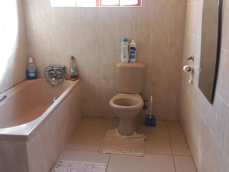 A functional bathroom featuring a built-in bathtub and toilet with neutral ceramic wall and floor tiling throughout.