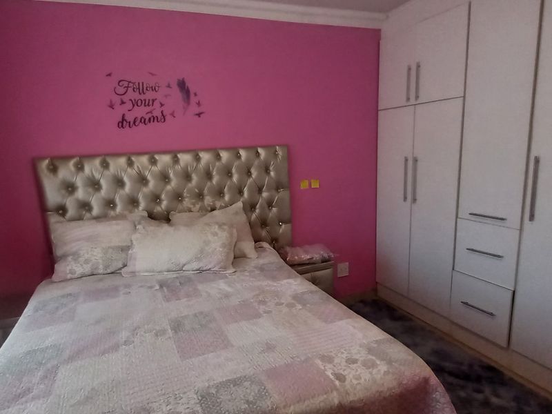 A bedroom featuring built-in wardrobes and coving, currently finished with bright pink wall paint.