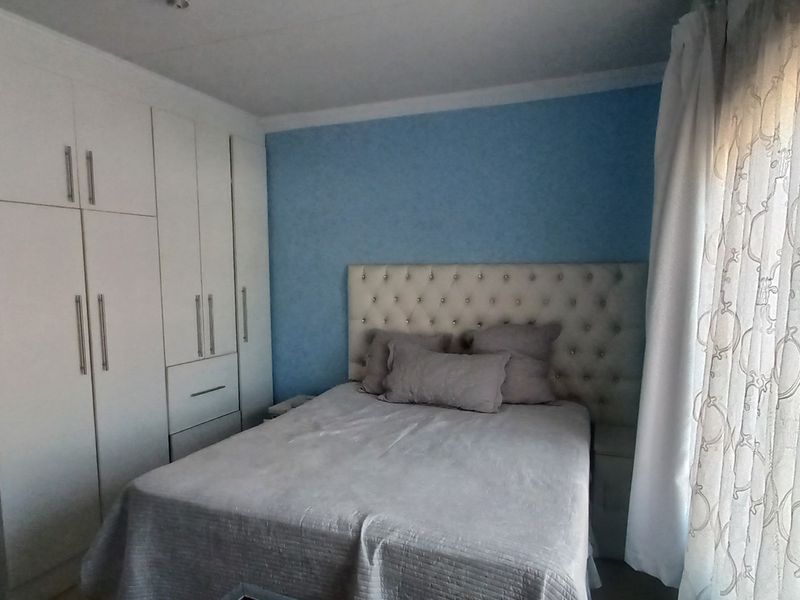 A well-maintained bedroom featuring built-in cupboards, blue painted walls, and natural light through the window.