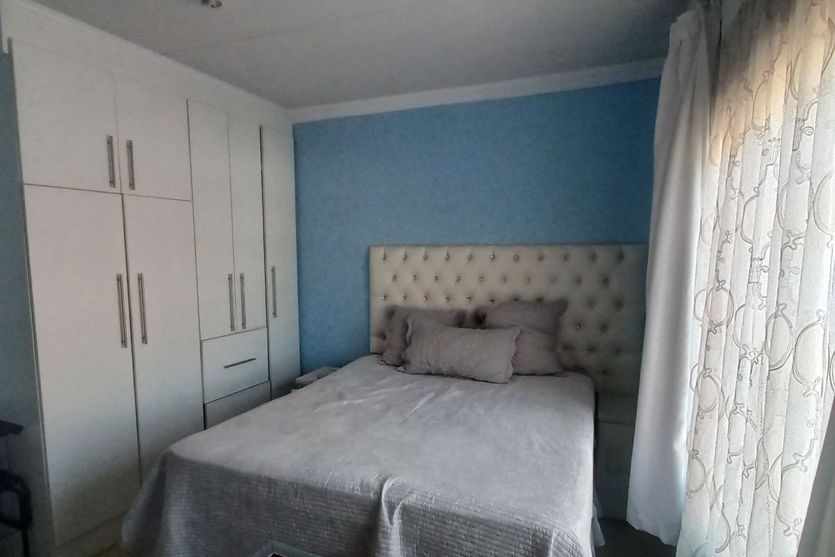 A well-maintained bedroom featuring built-in cupboards, blue painted walls, and natural light through the window.