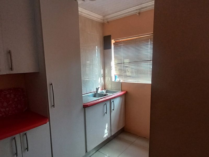 A functional scullery area featuring built-in cabinetry, a double sink, tiled splashbacks, and tiled flooring, providing additional utility space.