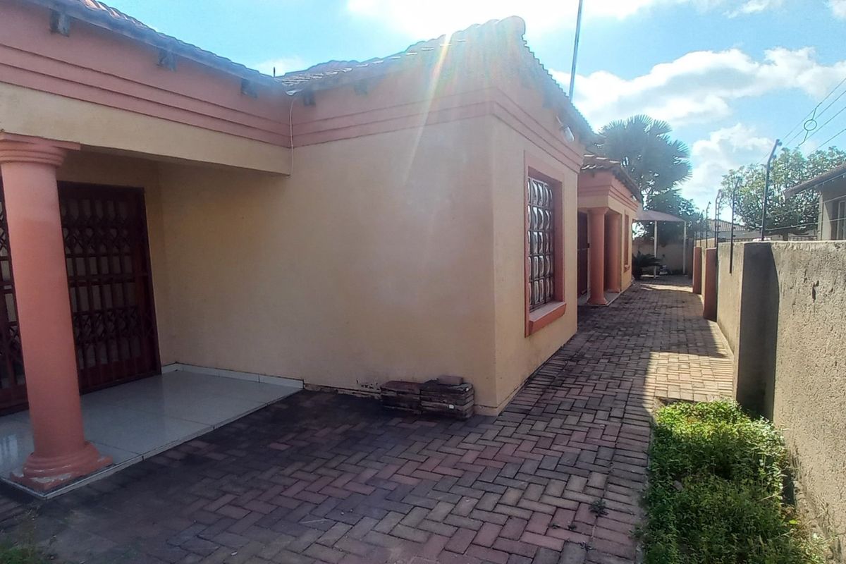 Rear exterior view of the house featuring a paved patio area, perimeter wall with electric fencing, and structural columns.