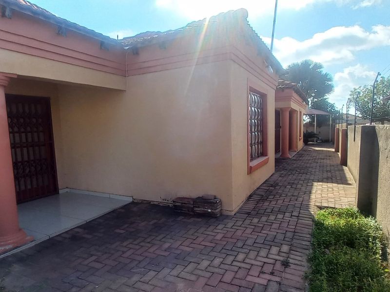 Rear exterior view of the house featuring a paved patio area, perimeter wall with electric fencing, and structural columns.