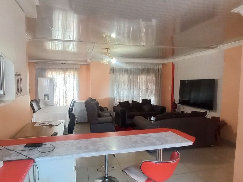 Open-plan living and kitchen area featuring a breakfast bar, tiled flooring, and coved ceilings, offering a functional layout for modern living.