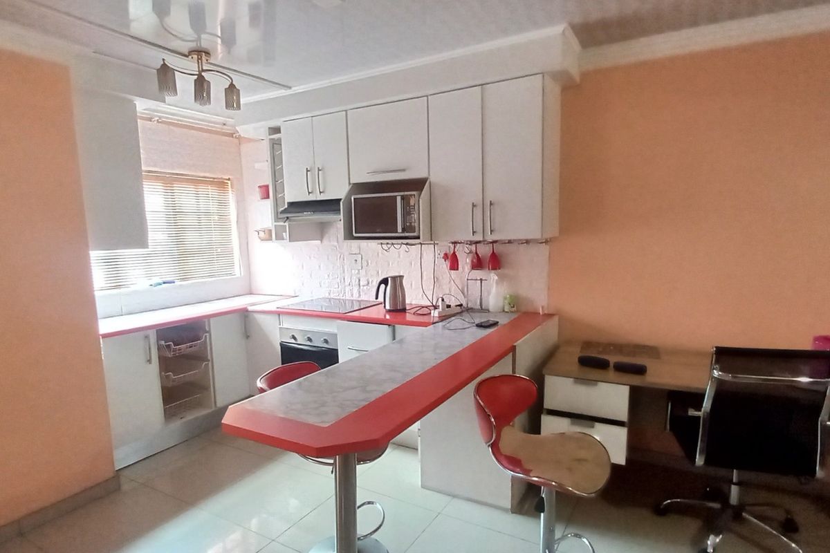 A functional kitchen featuring white cabinetry, a breakfast bar, built-in oven and hob, and an integrated desk area with tiled flooring.