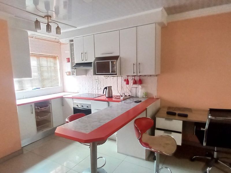 A functional kitchen featuring white cabinetry, a breakfast bar, built-in oven and hob, and an integrated desk area with tiled flooring.