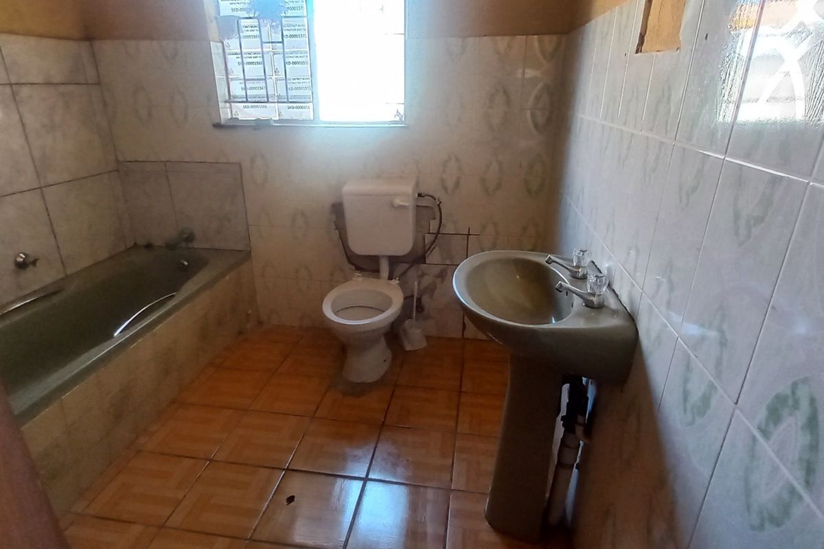 A dated bathroom featuring a bathtub, pedestal basin, and toilet with tiled finishes, requiring cosmetic updates and repairs to fixtures.