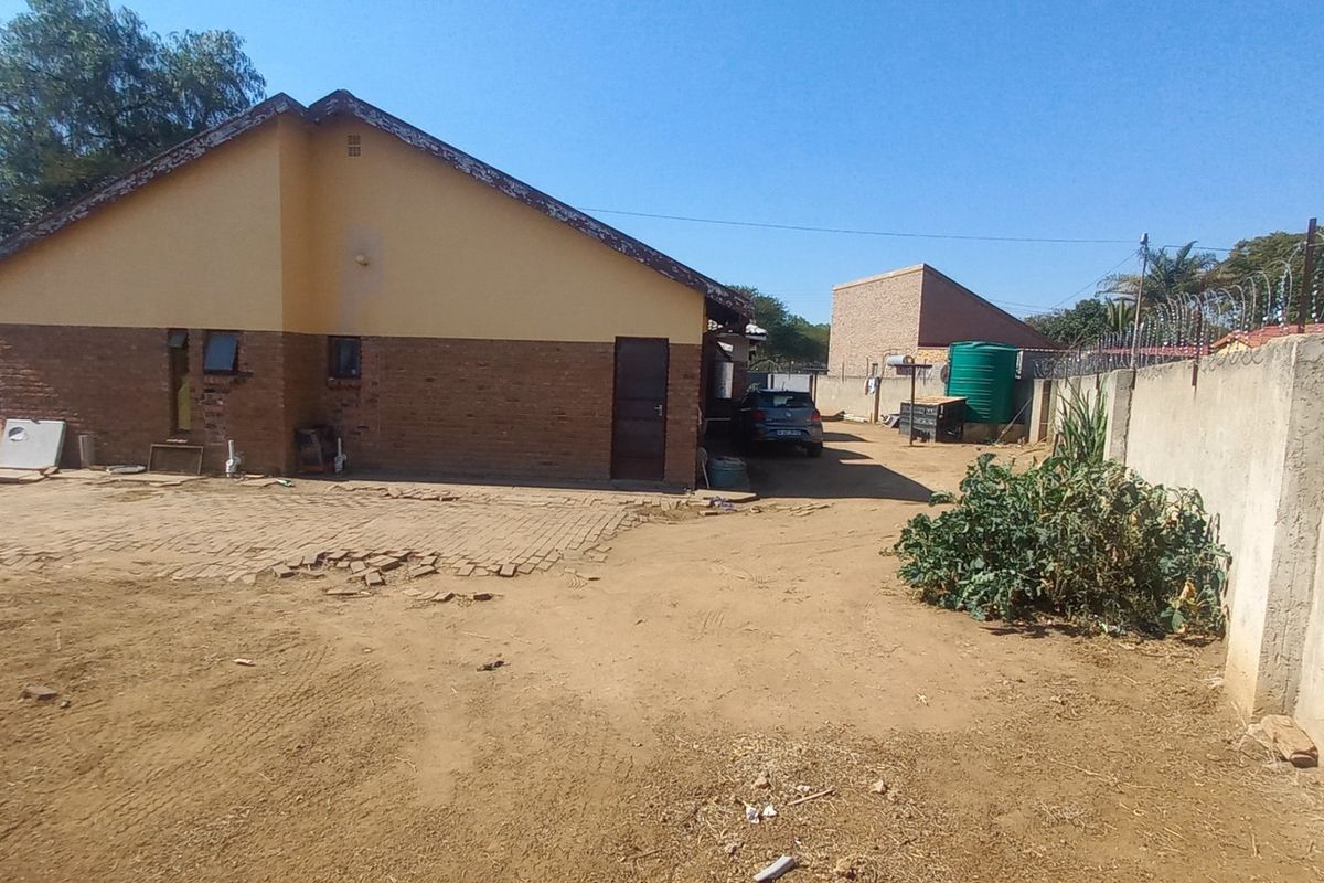 Rear view of the property featuring an exposed brick facade, paved area, water storage tank, and a secure boundary wall with razor wire.