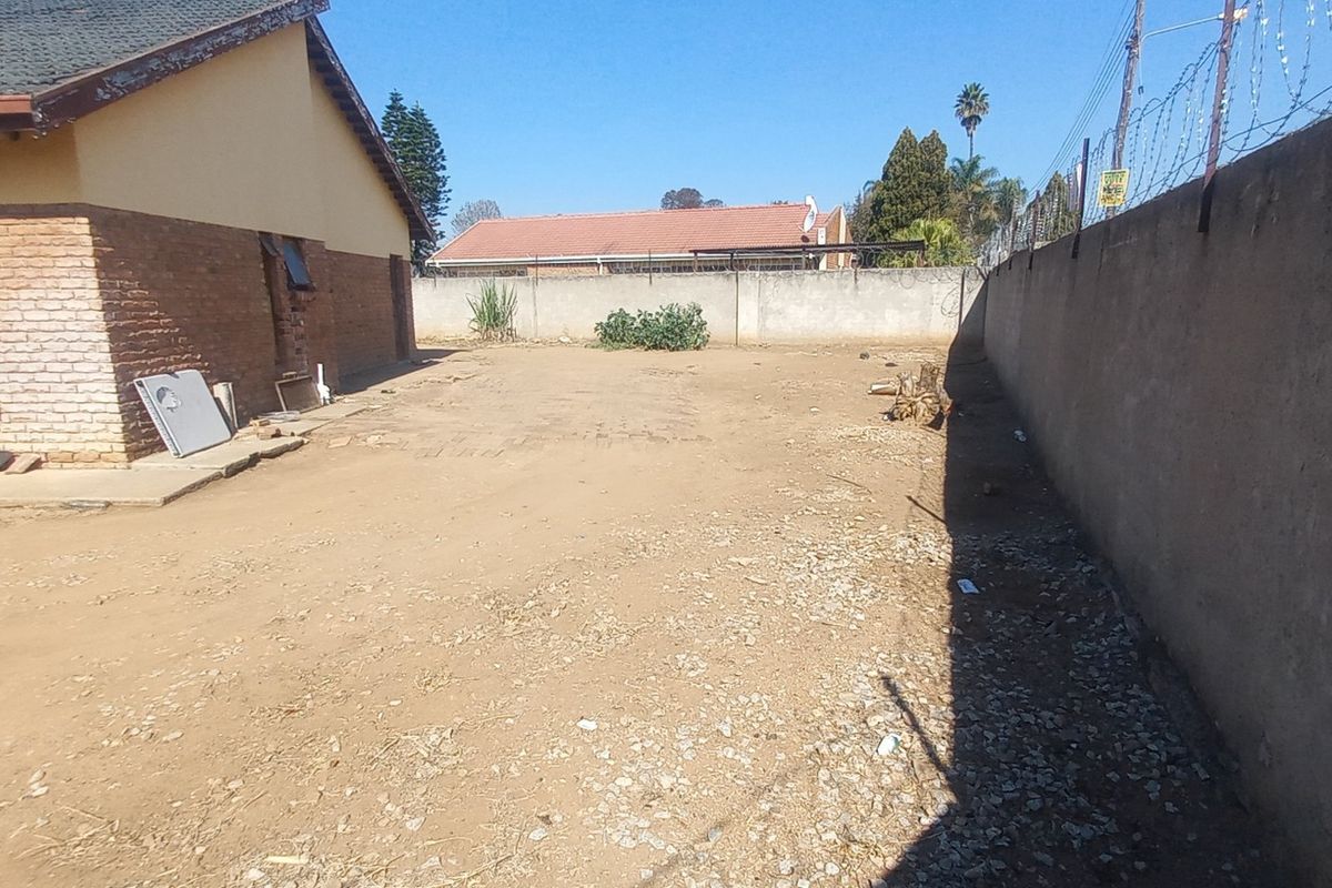 A spacious, unlandscaped rear yard area featuring a perimeter wall with security razor wire and a view of the house's brick exterior.