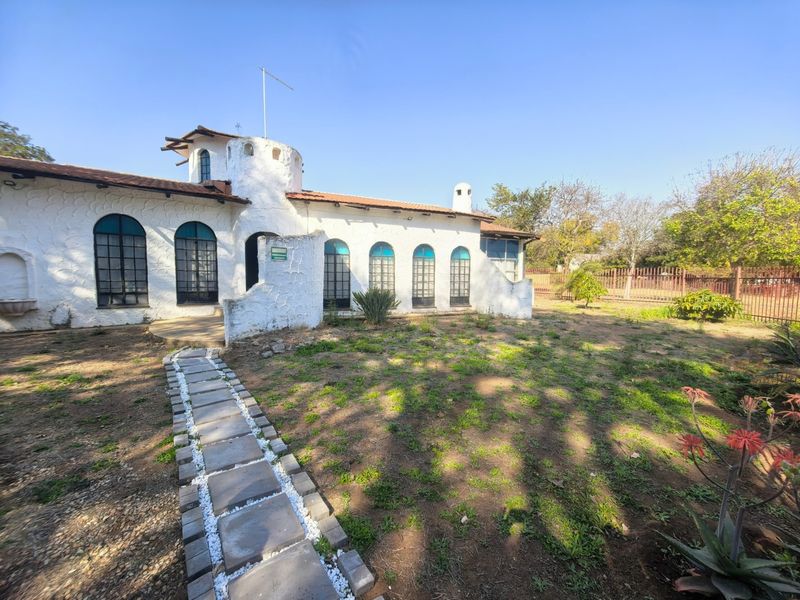 Rear view of a unique white-walled house featuring arched windows, a turret, and a stone pathway leading through the garden.