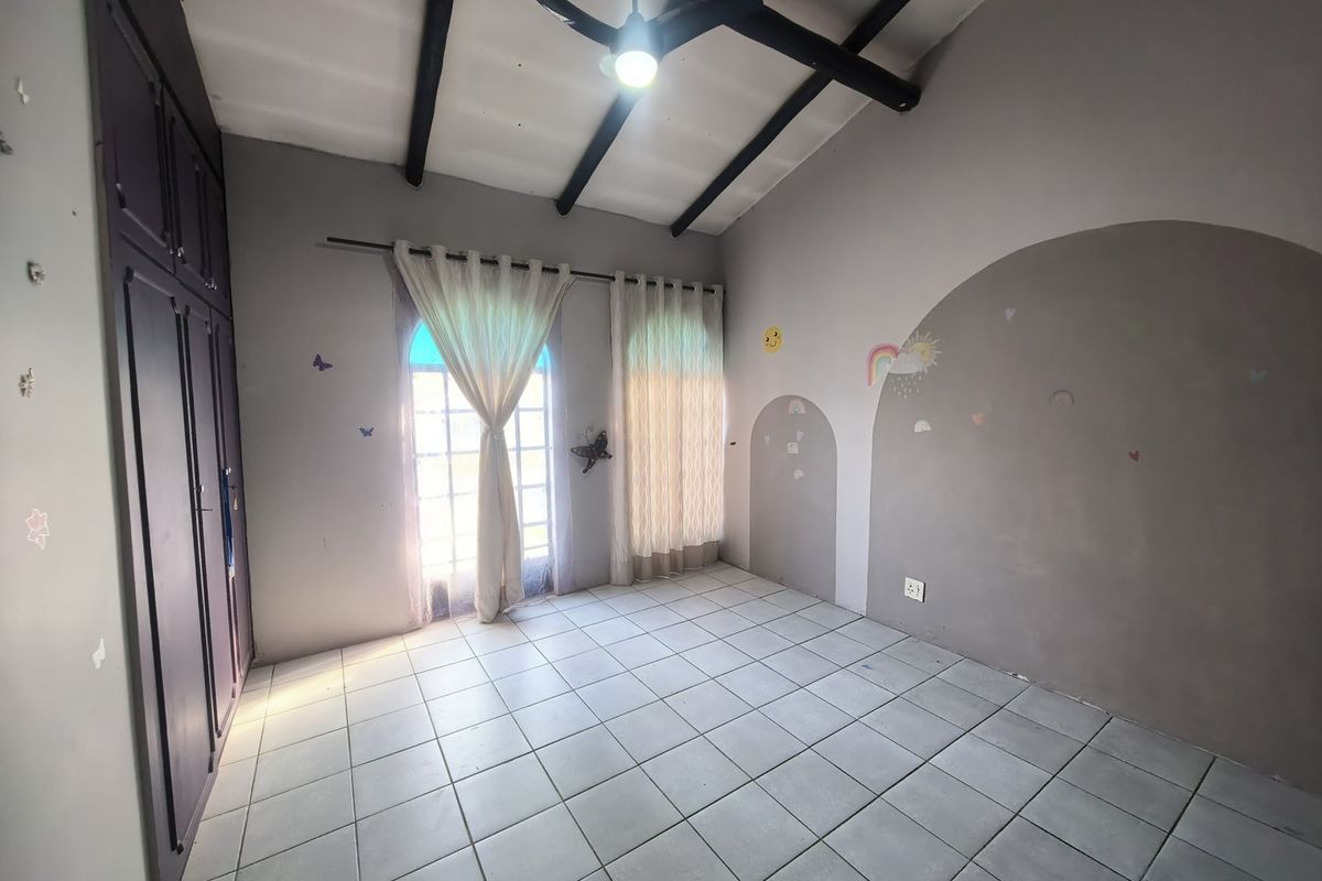 A spacious bedroom featuring tiled flooring, exposed ceiling beams, built-in cupboards, and double doors leading to the exterior.
