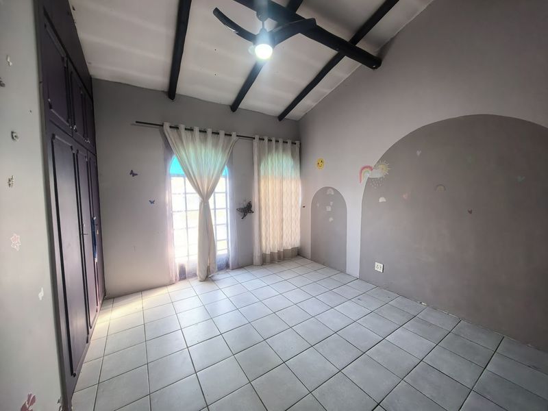 A spacious bedroom featuring tiled flooring, exposed ceiling beams, built-in cupboards, and double doors leading to the exterior.
