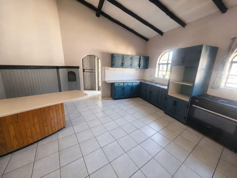 Spacious kitchen featuring exposed timber beams, ample built-in cabinetry, a breakfast bar, and tiled flooring, offering a functional layout ready for modernization.