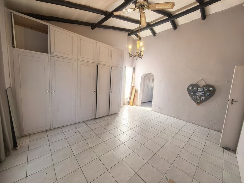 Spacious bedroom featuring built-in cupboards, exposed timber ceiling beams, and tiled flooring, offering a blank canvas for renovation and personalization.