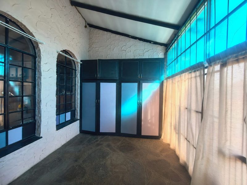 A sun-drenched enclosed patio featuring stone flooring, built-in storage cupboards, arched windows, and exposed ceiling rafters.
