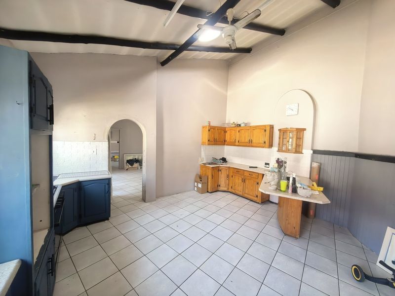 Spacious kitchen featuring tiled flooring, exposed ceiling beams, and built-in wooden cabinetry with an arched doorway leading to adjacent living areas.