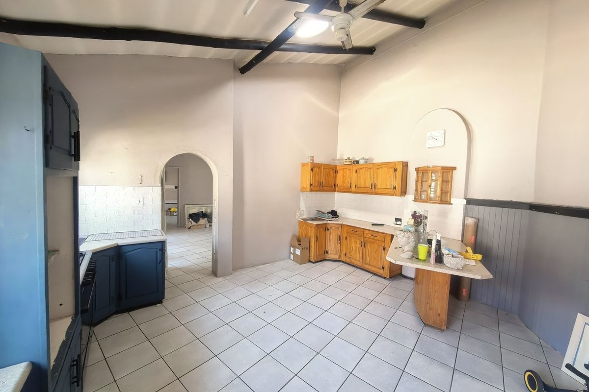 Spacious kitchen featuring tiled flooring, exposed ceiling beams, and built-in wooden cabinetry with an arched doorway leading to adjacent living areas.
