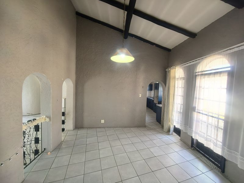Spacious living area featuring high vaulted ceilings with exposed timber beams, tiled flooring, and distinctive arched architectural details leading to adjacent rooms.