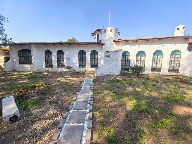 Rear elevation of a unique property featuring a turret, arched windows, and a stone pathway leading to the main structure.