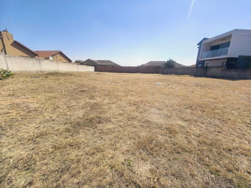 A vacant residential plot featuring dry grass and enclosed by perimeter boundary walls, situated in a developed suburban neighborhood.