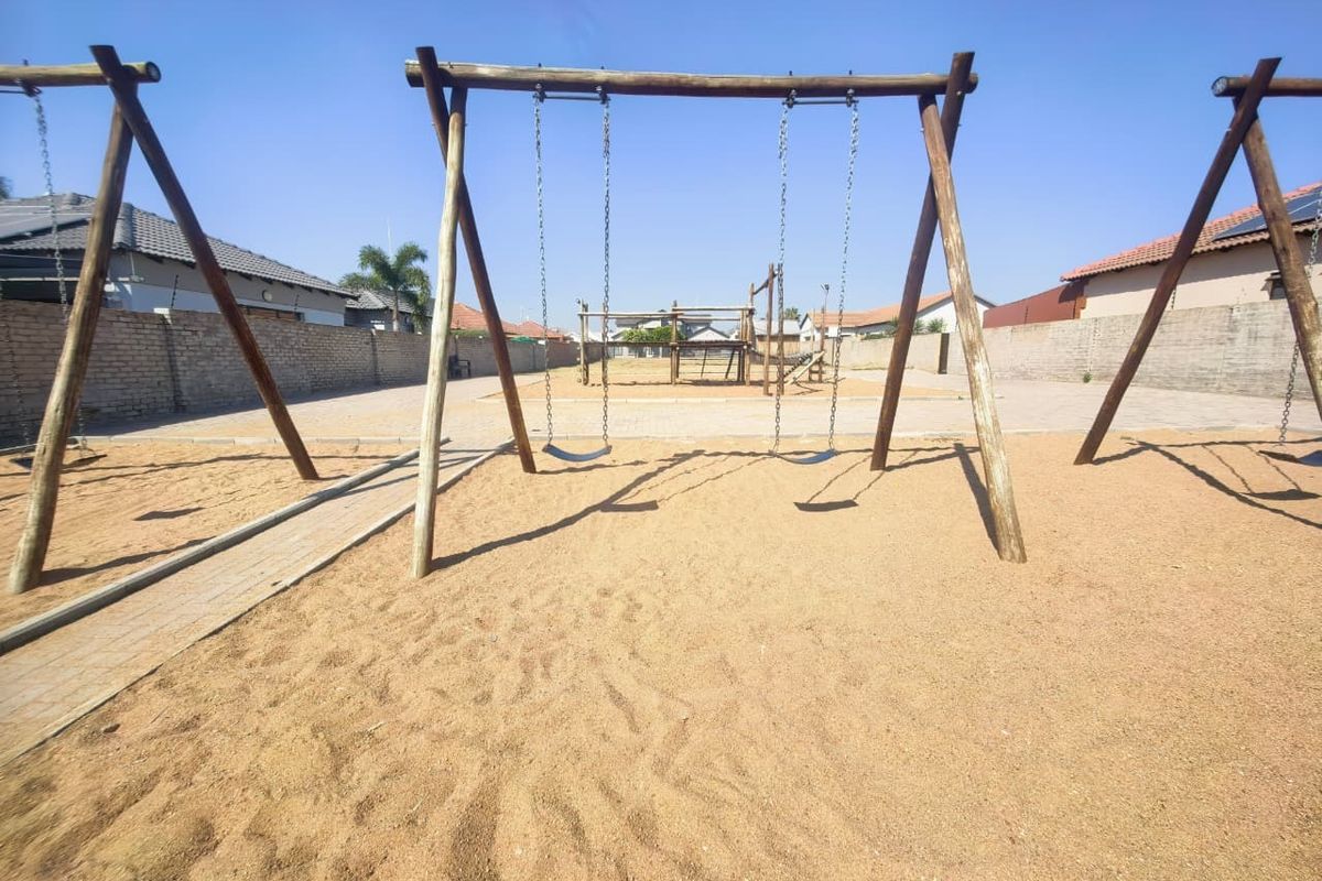 A communal outdoor play area featuring a swing set, sand pit, and paved pathways, enclosed by perimeter brick walls.