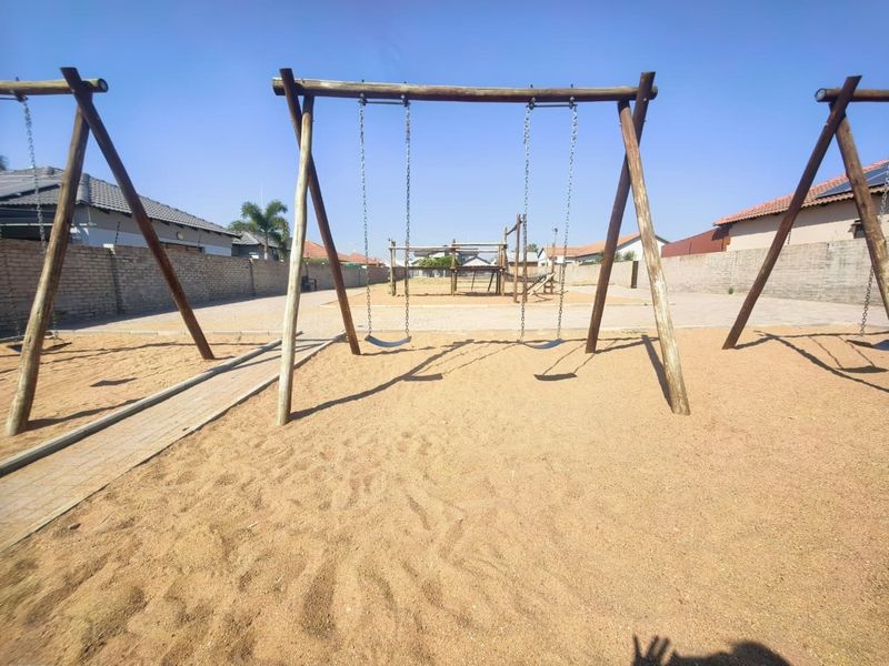 A communal outdoor play area featuring a swing set, sand pit, and paved pathways, enclosed by perimeter brick walls.