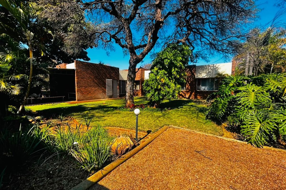 A view of the rear garden featuring mature trees, established landscaping, and a brick-faced building exterior.