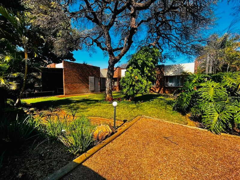 A view of the rear garden featuring mature trees, established landscaping, and a brick-faced building exterior.