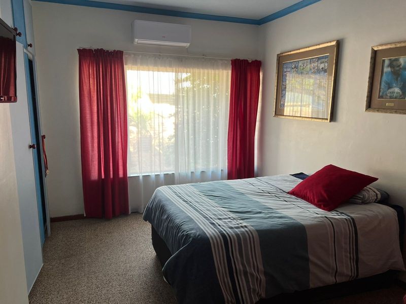 A functional bedroom featuring carpet flooring, a built-in wardrobe, and a wall-mounted split-system air conditioning unit.