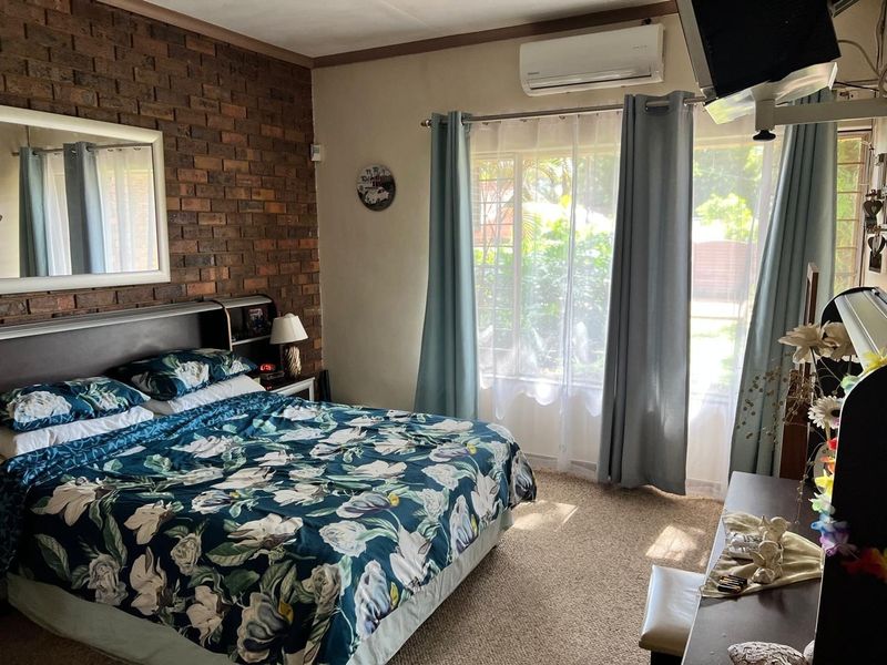 A bedroom featuring an exposed brick wall, carpeted flooring, and a wall-mounted split-system air conditioner.