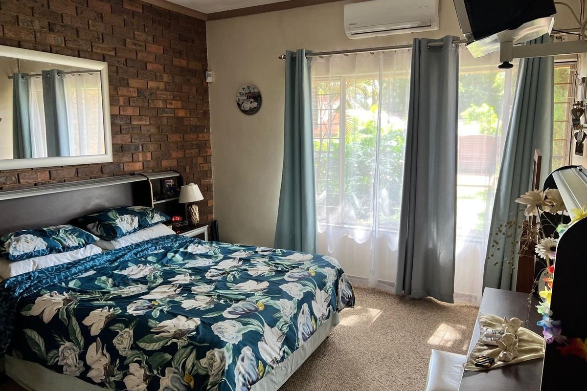 A bedroom featuring an exposed brick wall, carpeted flooring, and a wall-mounted split-system air conditioner.