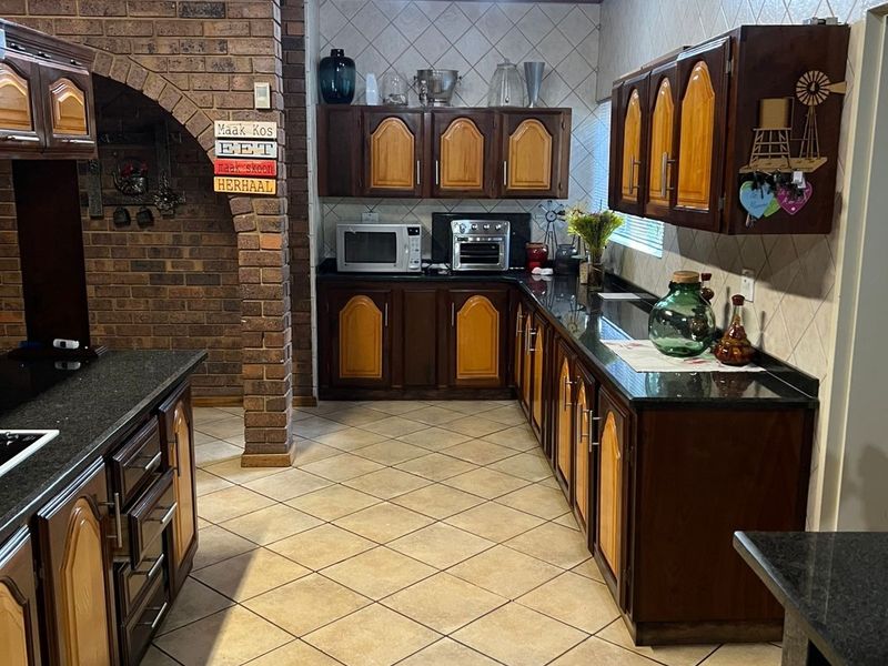 A traditional kitchen featuring dark wood cabinetry, granite countertops, a brick feature wall, and a timber-clad ceiling with tiled flooring.