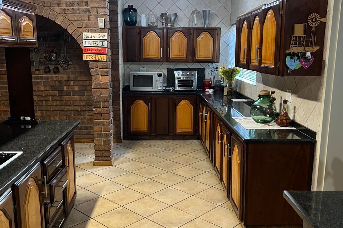 A traditional kitchen featuring dark wood cabinetry, granite countertops, a brick feature wall, and a timber-clad ceiling with tiled flooring.