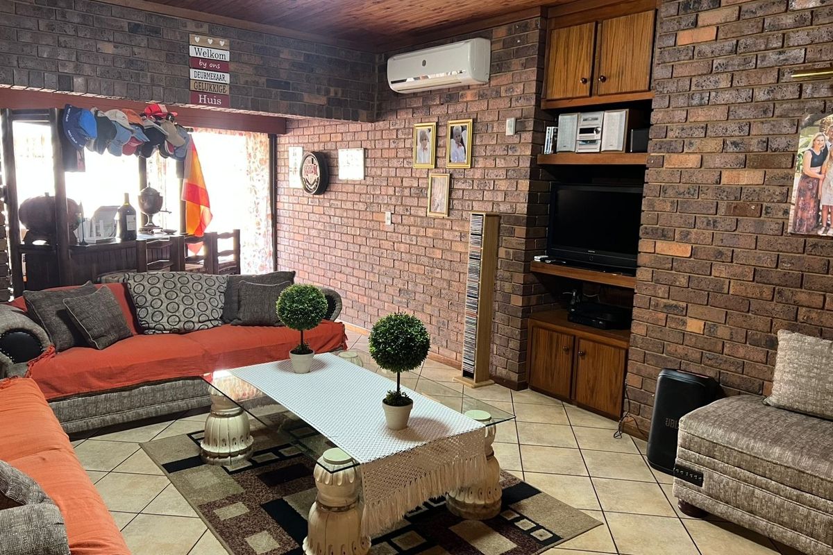 A living room featuring exposed brick walls, a timber-clad ceiling, ceramic floor tiles, and built-in wooden cabinetry with an integrated air conditioning unit.