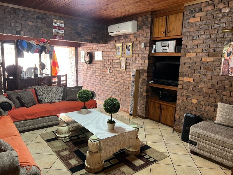 A living room featuring exposed brick walls, a timber-clad ceiling, ceramic floor tiles, and built-in wooden cabinetry with an integrated air conditioning unit.