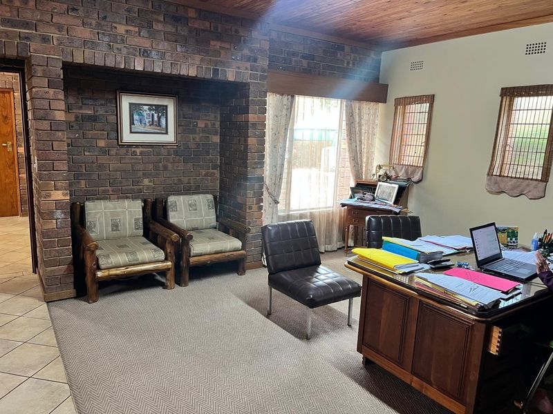 A home office featuring an exposed brick feature wall, timber ceiling, and a mix of tiled and carpeted flooring.