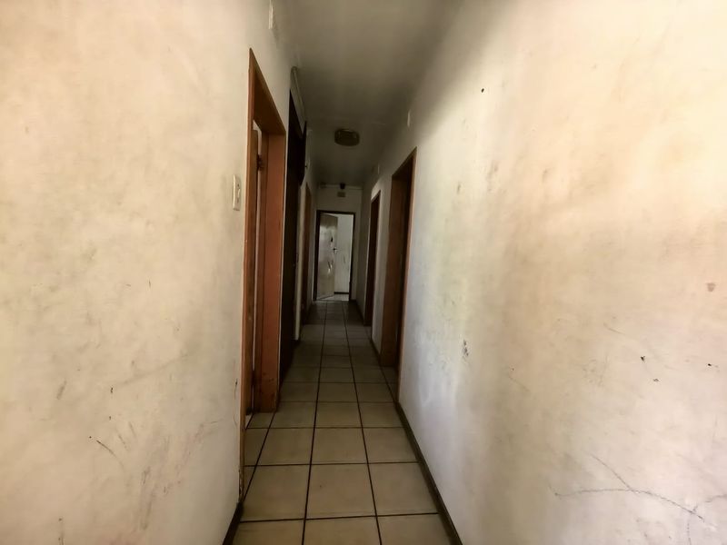 A narrow hallway featuring tiled flooring and wooden door frames, currently showing significant wear and staining on the walls.