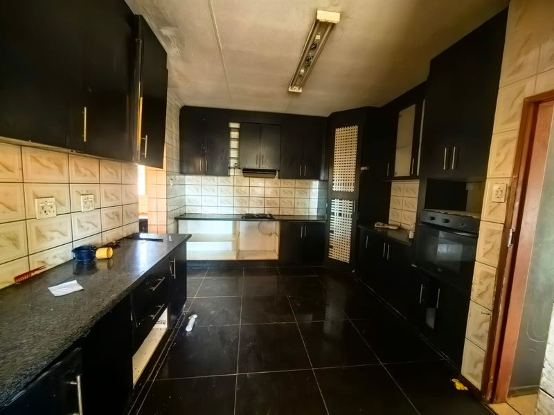 A spacious kitchen featuring dark built-in cabinetry, granite countertops, and integrated appliances, currently in need of cosmetic updates and repairs.