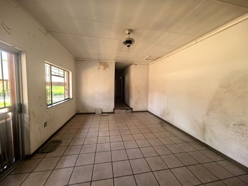 An empty living room featuring tiled flooring, a ceiling fan, and sliding door access, requiring significant cosmetic renovation and wall repairs.