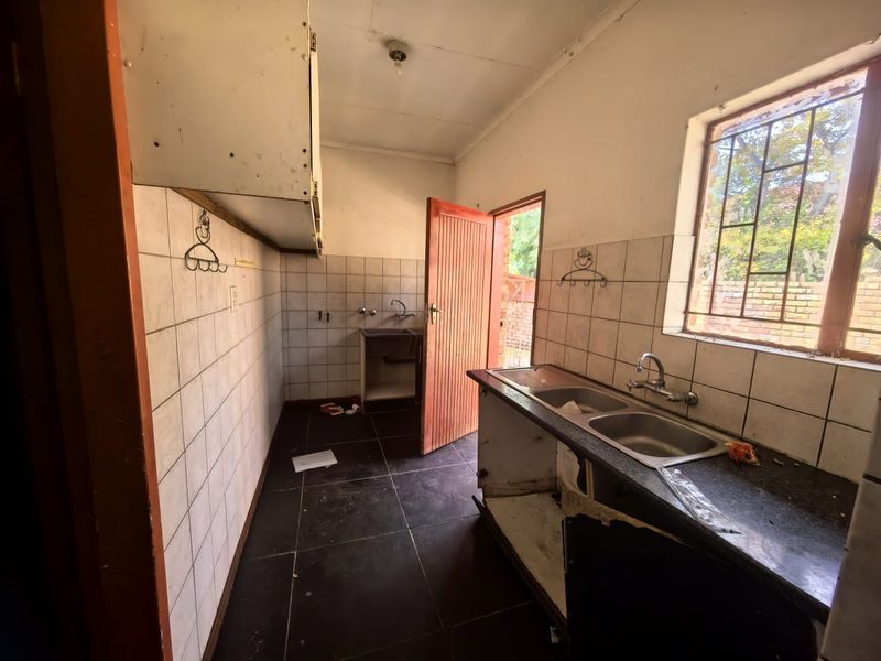 A dated kitchen space featuring tiled walls, dark floor tiles, and a double bowl sink, requiring renovation to modernize the cabinetry and finishes.