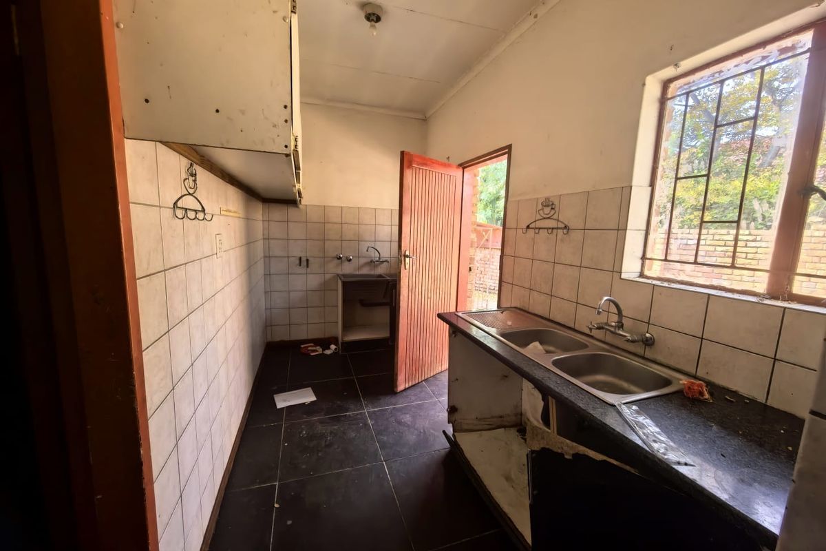 A dated kitchen space featuring tiled walls, dark floor tiles, and a double bowl sink, requiring renovation to modernize the cabinetry and finishes.