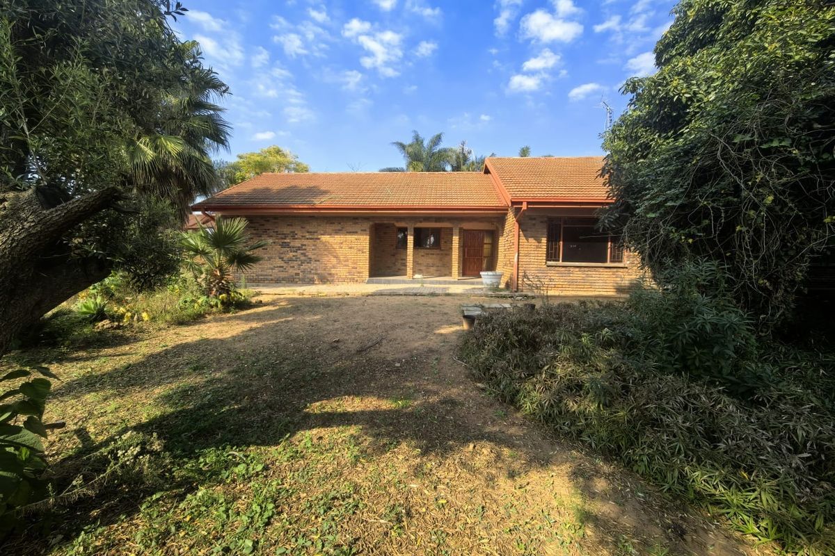 A rear view of a single-story face brick house featuring a covered patio, tiled roof, and established garden surroundings.