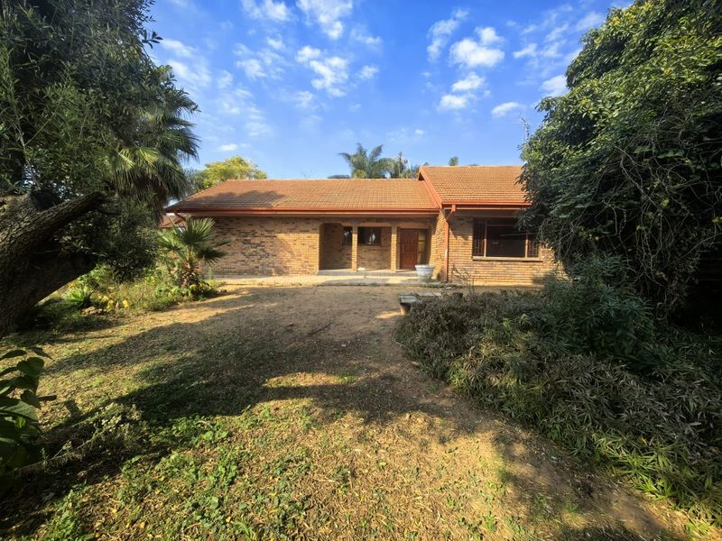A rear view of a single-story face brick house featuring a covered patio, tiled roof, and established garden surroundings.