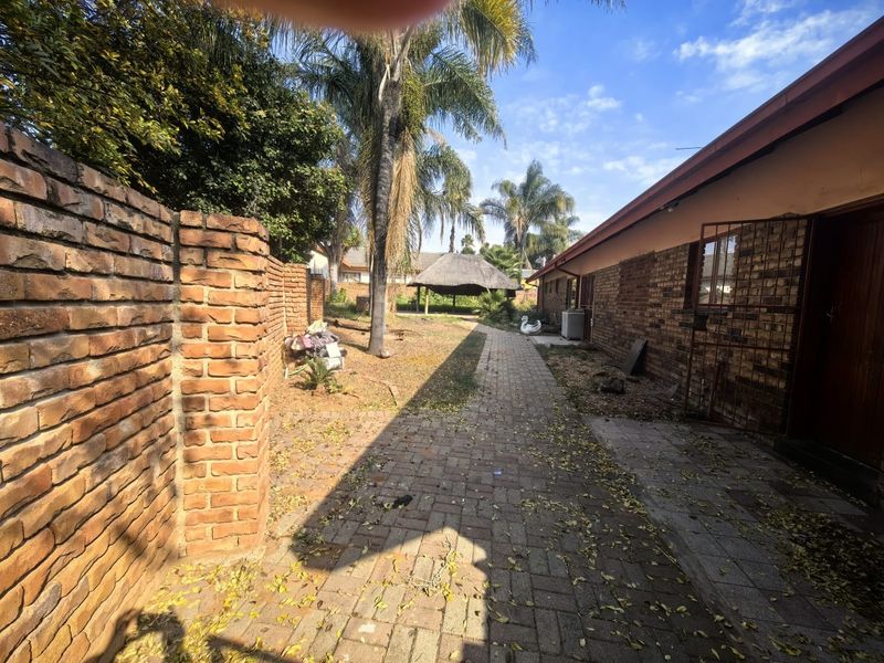 Rear garden area featuring a paved walkway, facebrick exterior walls, and a detached thatch lapa structure in the background.