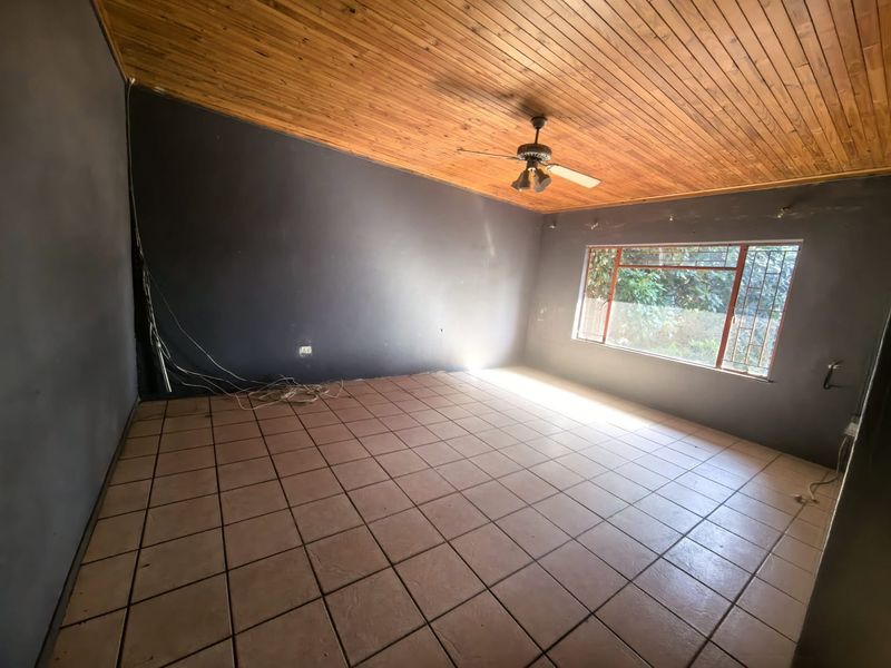An empty living room featuring a timber-clad ceiling, tiled flooring, and a large window with security bars, requiring minor cosmetic updates.