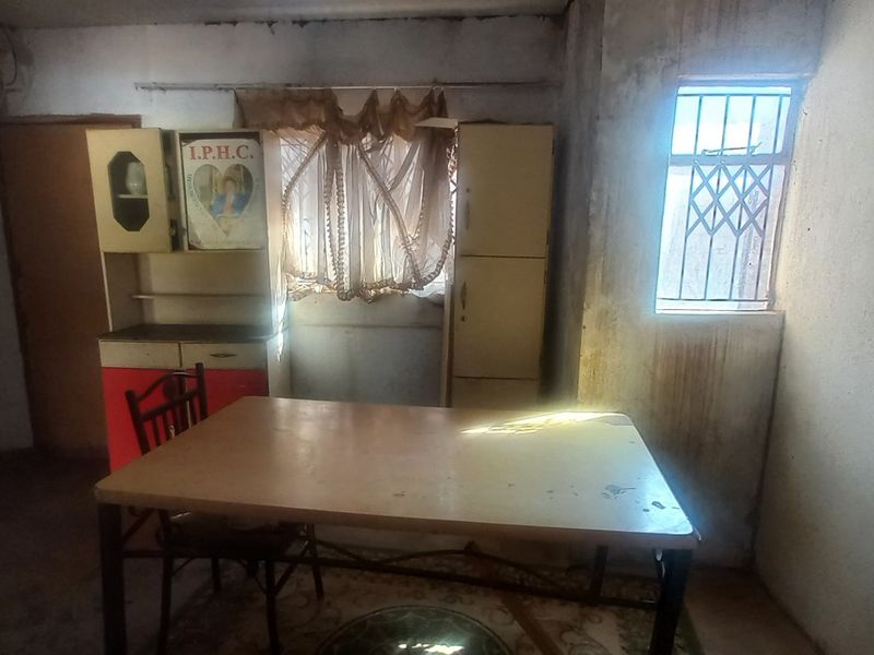 A dining area featuring a window with security bars and visible wall deterioration, requiring cosmetic updates and repairs to improve the overall condition.