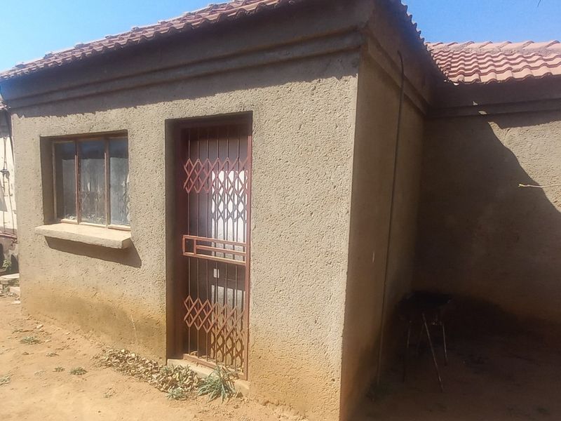 Rear view of a single-story house featuring a tiled roof, security gate, and weathered exterior plaster walls.